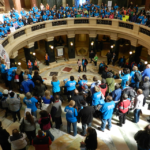 People in blue t-shirts standing around the rotunda at the Wisconsin Capitol on Disability Advocacy Day