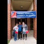Three people standing in front of building with a Project Homeless Connect banner hanging in the doorway